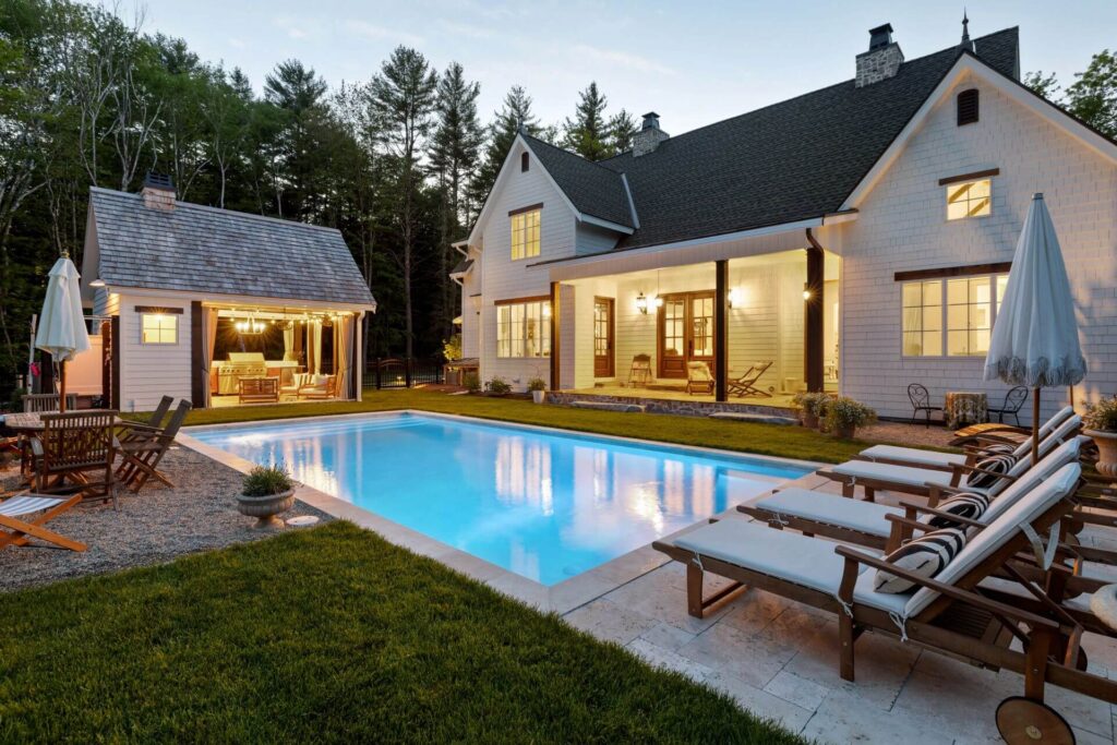 Elegant backyard with a swimming pool, lounge chairs, and a cozy outdoor living space featuring a grill and seating area, surrounded by lush greenery, ideal for landscaping inspiration.