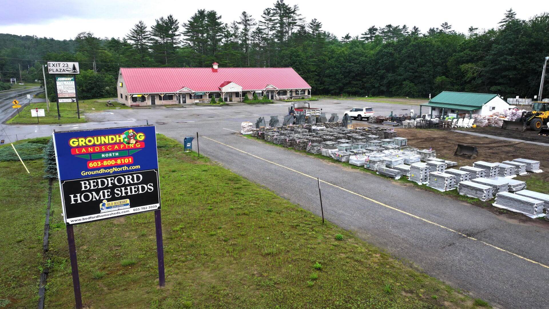 Groundhog Landscaping sign in front of a landscape materials center with stacks of stone and equipment, showcasing landscaping services and products for home improvement.