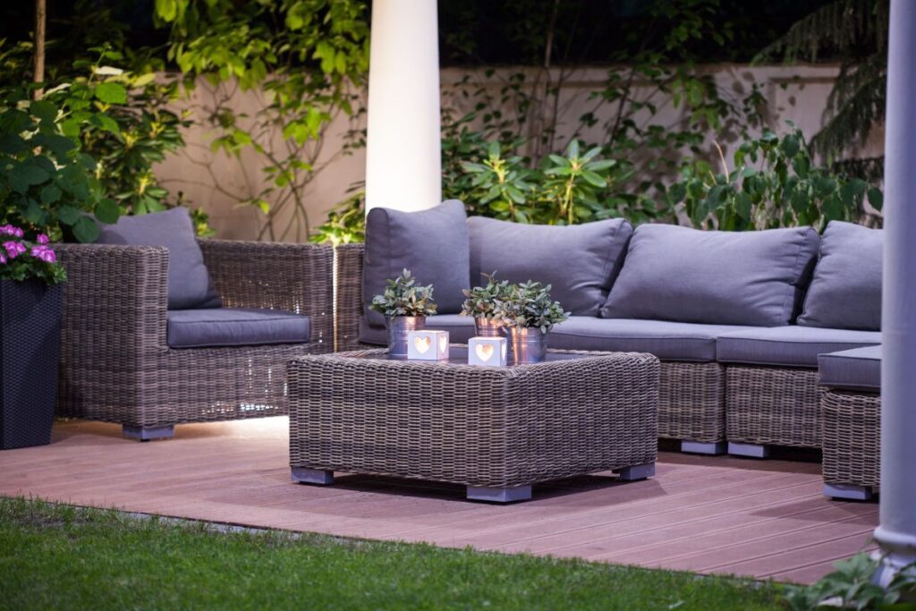Outdoor seating area with gray wicker furniture, decorative potted plants, and soft lighting, enhancing backyard ambiance and inviting outdoor living.