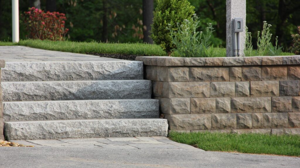 Granite steps leading to a landscaped area, showcasing durability and elegance, complemented by a stone wall and greenery, highlighting granite's role in New Hampshire landscaping.
