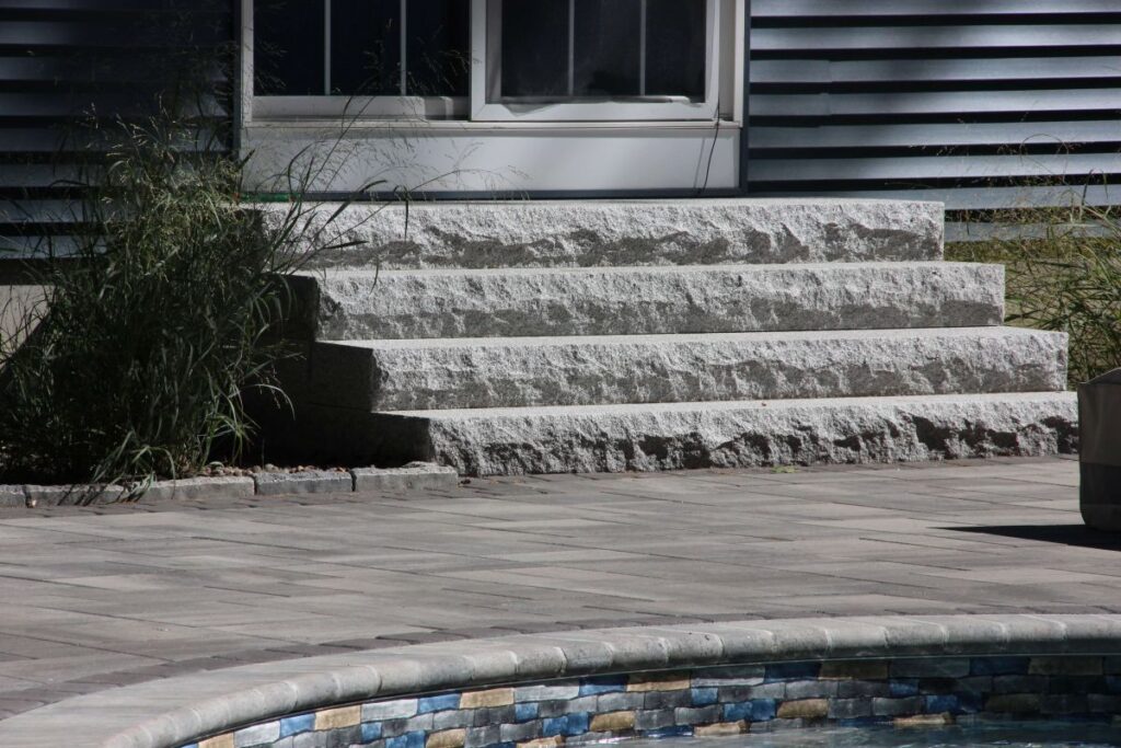 Granite steps leading to a New England home, showcasing durable and elegant craftsmanship, surrounded by landscaping elements.