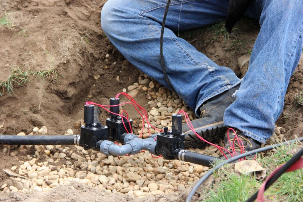 Professional installing irrigation valves with wiring in a dug trench, showcasing components for efficient landscape watering.