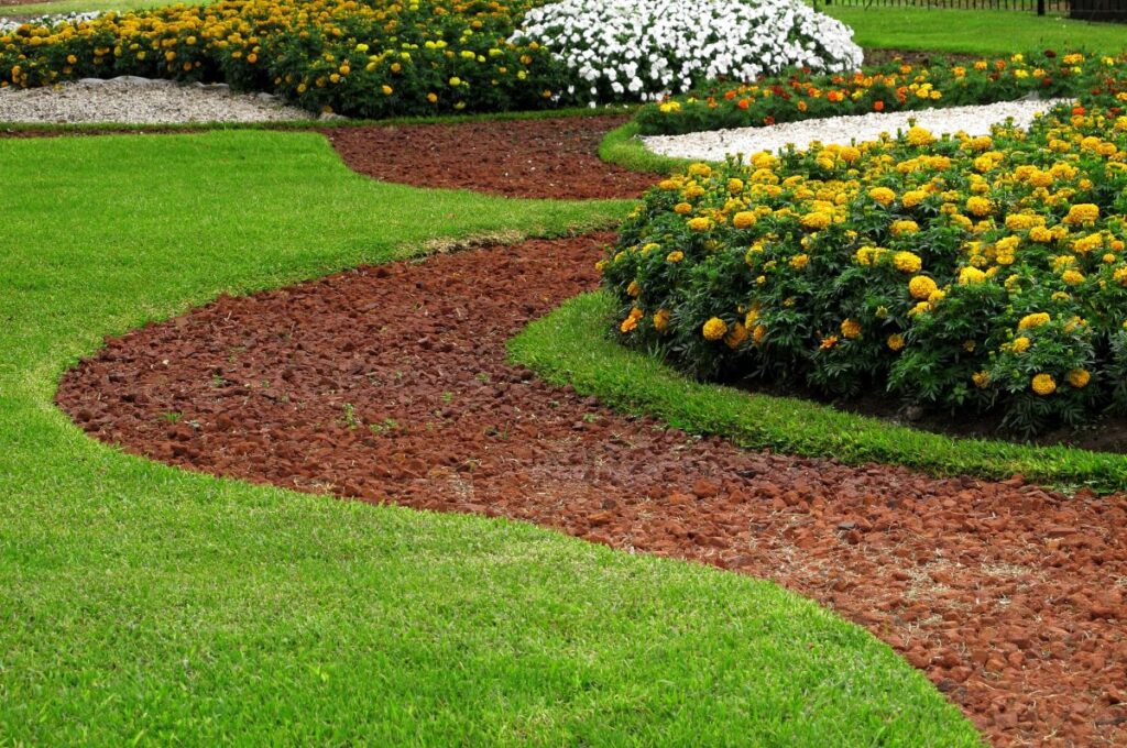 Colorful flower beds with marigolds and white blooms framed by a winding mulch path, showcasing vibrant landscaping enhancements for curb appeal.