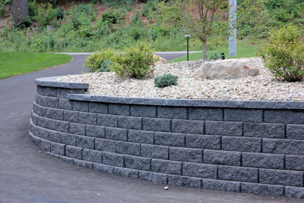 Curved granite retaining wall with polished stone surface, surrounded by decorative gravel and low-maintenance shrubs, enhancing landscape aesthetics and curb appeal.