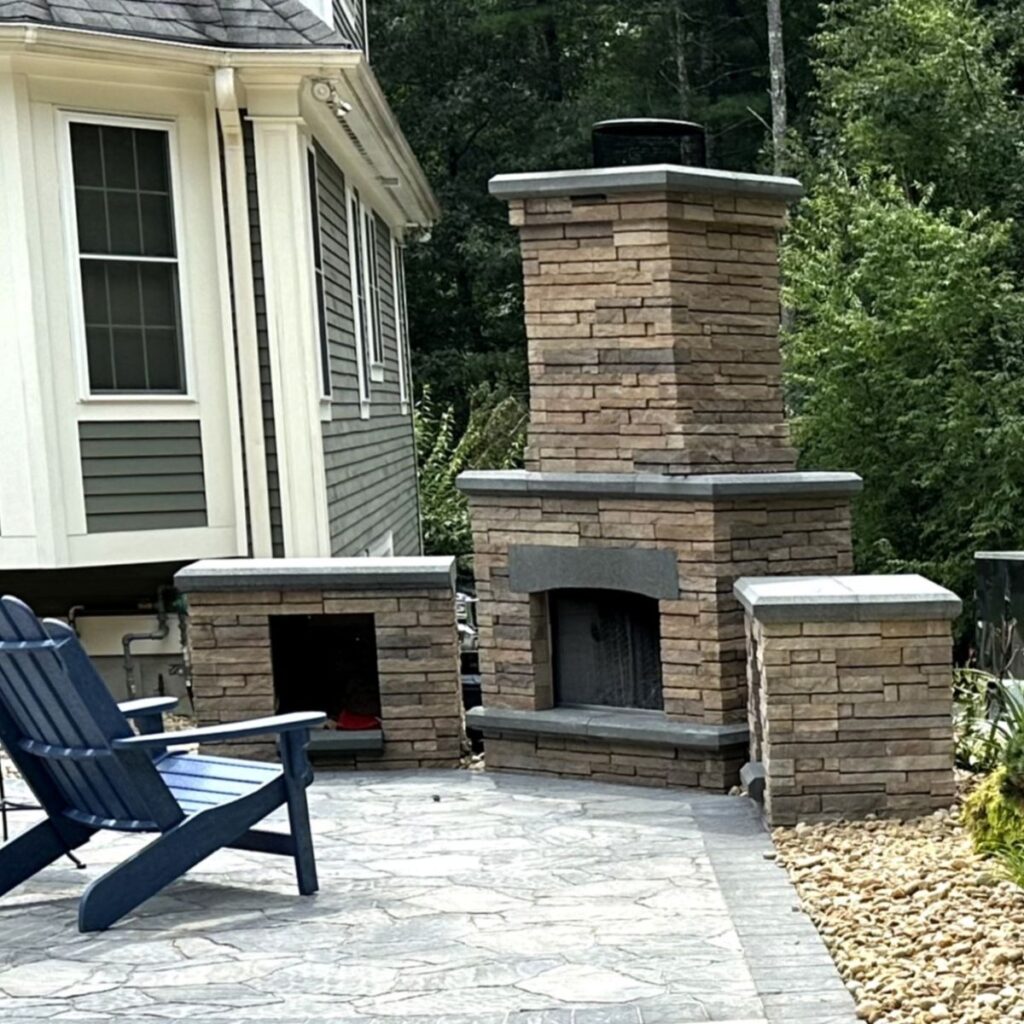 Outdoor living space featuring a stone fireplace, granite accents, and a blue Adirondack chair, ideal for summer hardscaping projects by Groundhog Landscaping in New Hampshire.
