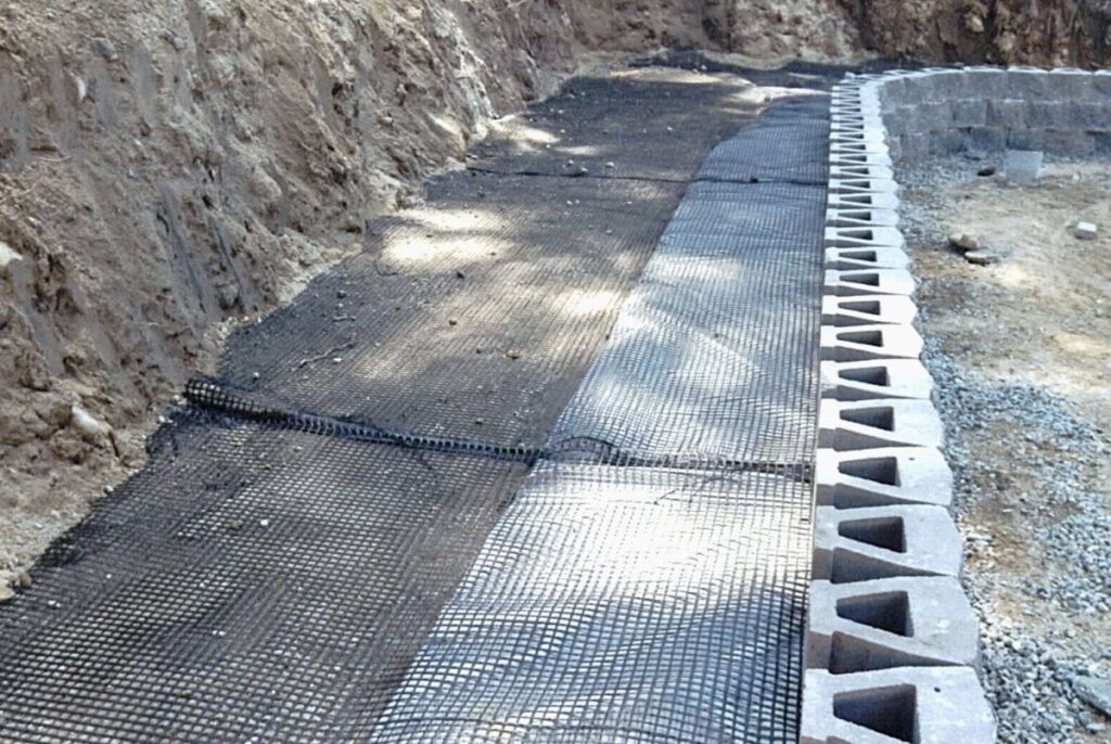 Geogrid reinforcement installed behind a retaining wall, showcasing proper drainage and foundation preparation for durable hardscape projects.