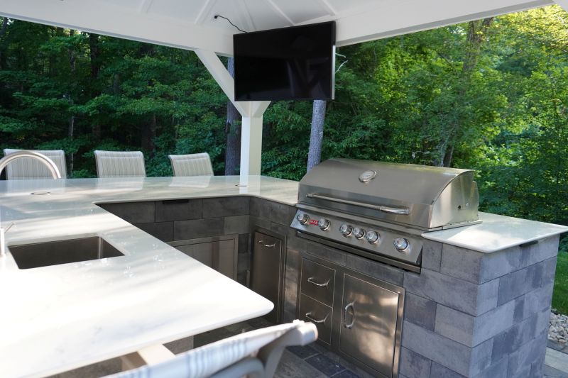 Outdoor kitchen featuring stainless steel grill, granite countertop, and seating area, surrounded by greenery, ideal for entertaining and enhancing outdoor living spaces.