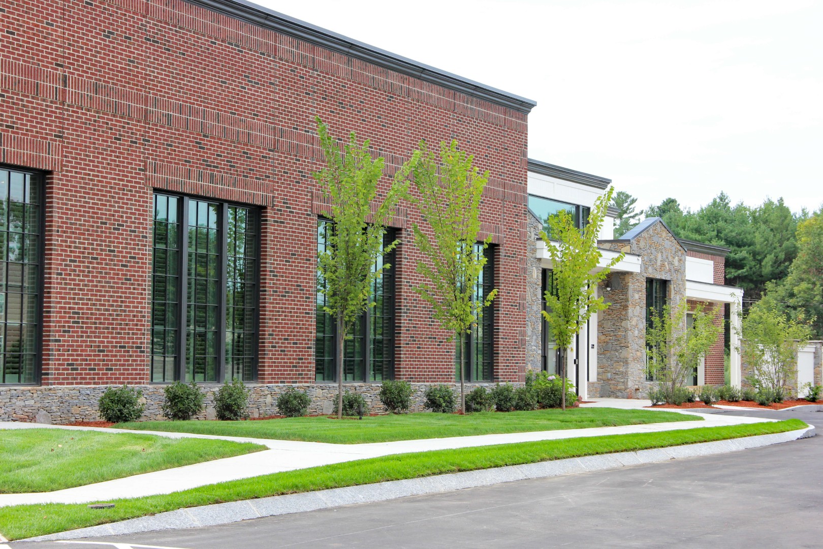 Commercial building exterior with landscaped lawn, featuring manicured grass, young trees, and stone accents, representing professional landscape maintenance services by Groundhog Landscaping Inc.
