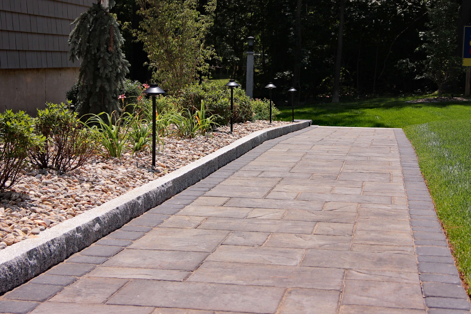 Paved walkway with retaining wall, bordered by garden lighting and landscaping, enhancing outdoor space usability and aesthetic appeal in Salem, NH.
