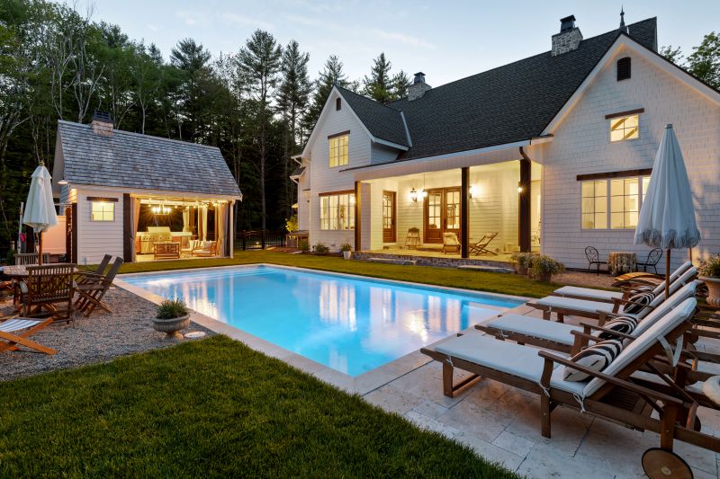 Elegant backyard with a swimming pool, modern home, outdoor seating area, and landscaped garden in Exeter, NH, showcasing Groundhog Landscaping's design expertise.