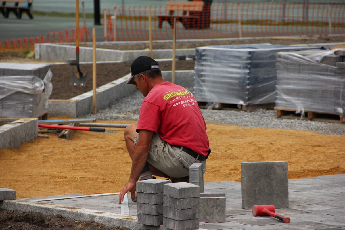 Groundhog Landscaping worker laying pavers in outdoor hardscaping project, featuring granite elements and construction tools in Milford, NH.