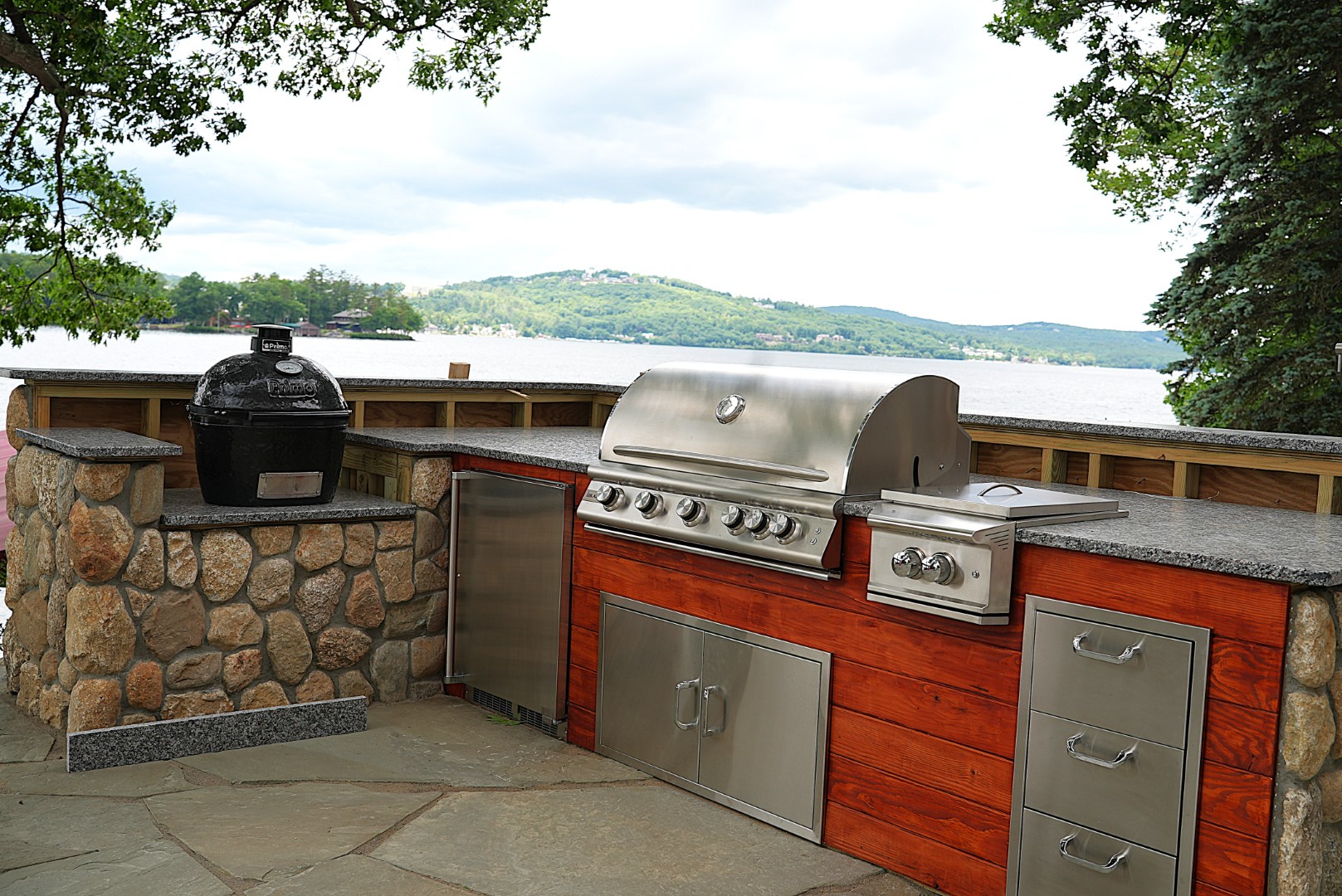 Outdoor kitchen featuring a stainless steel grill and stone cabinetry, set against a scenic lake view, designed for entertaining and enhancing outdoor living spaces.