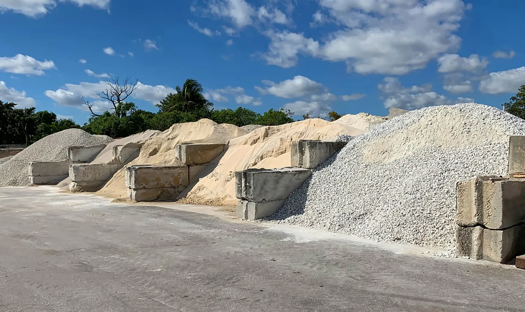 Piles of gravel, sand, and stone materials in a landscaping supply yard, showcasing delivery options for Groundhog Landscaping in Derry, NH.