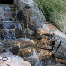 Natural stone waterfall feature with cascading water, surrounded by stacked stones, enhancing the Londonderry Pool Patio landscape design.