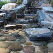 Stone steps leading to a pool area, surrounded by natural stone and pebbles, showcasing a hardscaping design for outdoor living spaces.